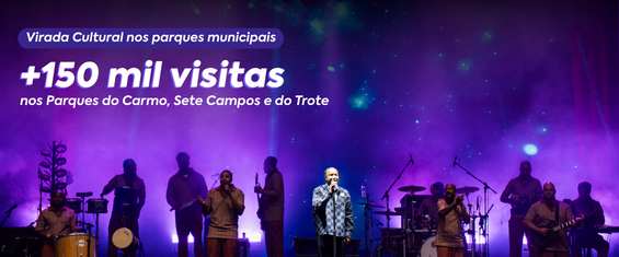 Palco de show ao ar livre durante a noite, iluminado por luzes roxas e azuis. Ao centro, um cantor de camisa estampada segura o microfone enquanto músicos tocam instrumentos ao redor, formando silhuetas contra o fundo iluminado. No topo esquerdo da imagem, há o texto em branco: “Virada Cultural nos parques municipais” e, em destaque, “+150 mil visitas nos Parques do Carmo, Sete Campos e do Trote”. O ambiente transmite clima de festival cultural com grande produção de luz e música ao vivo.